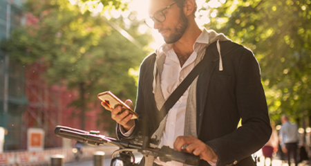 Mann steht neben seinem Fahrrad und hält ein Handy in der Hand