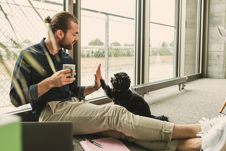Mann spielt mit einem schwarzen Hund und hält eine Tasse in der Hand 