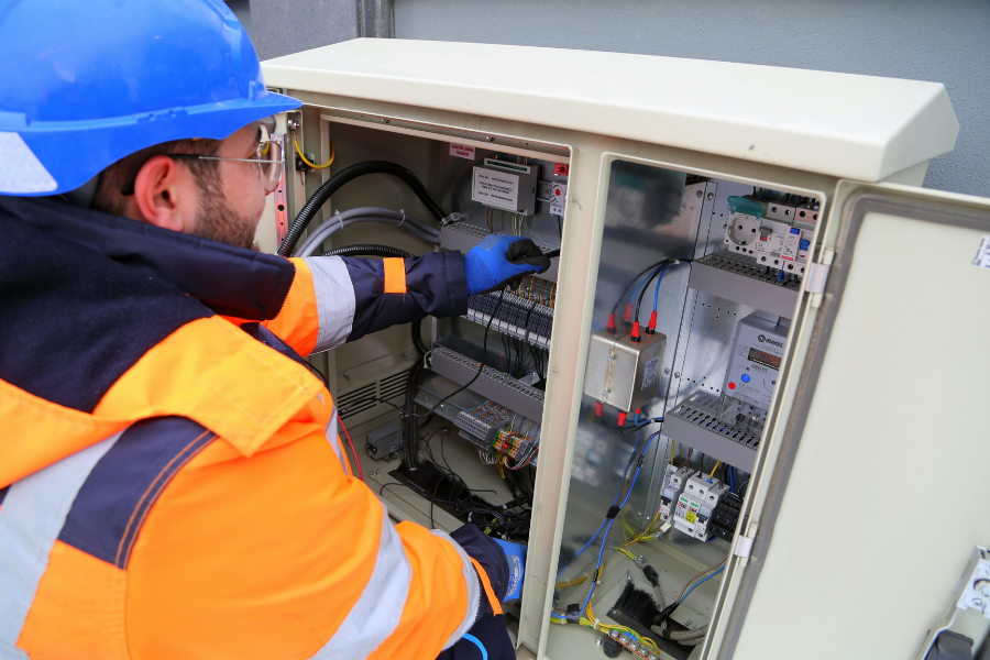 Elektroniker in Schutzkleidung und Helm arbeitet an einem Schaltschrank mit elektrischen Komponenten.