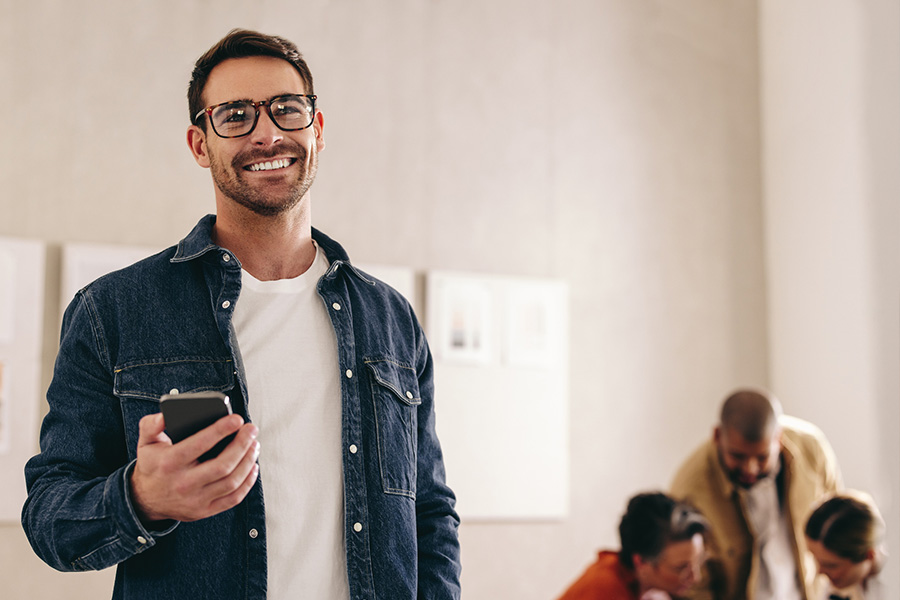 Ein Mann steht mit seinem Smartphone in der Hand und lächelt