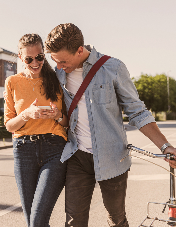 Ein Mann und eine Frau gehen zusammen in der Sonne und schauen auf ein Smartphone