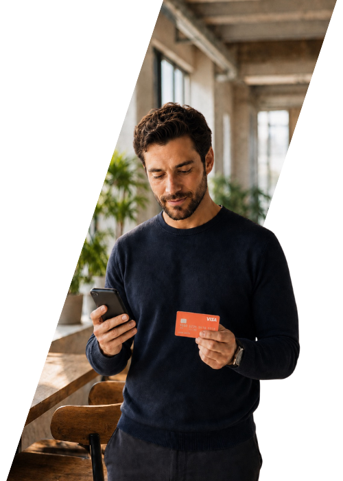 Mann hält eine orangefarbene Visa-Karte und schaut auf sein Smartphone.