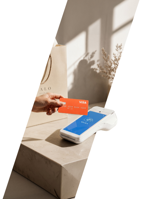 Hand hält eine orangefarbene Visa-Karte an ein weißes kontaktloses Kartenterminal von vobapay.